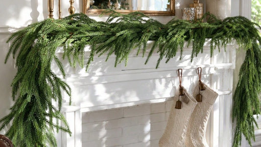Faux pine garland draped across a white fireplace mantel above two knit stockings